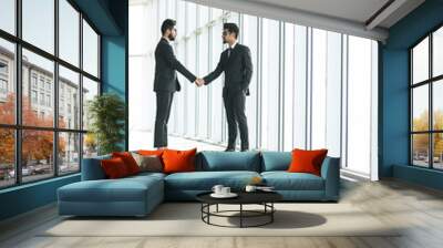 Two indian businessmen shaking hands standing at big window with urban cityscape, confident business partners handshaking in office, forming good relations, establish partnership, support, help.  Wall mural